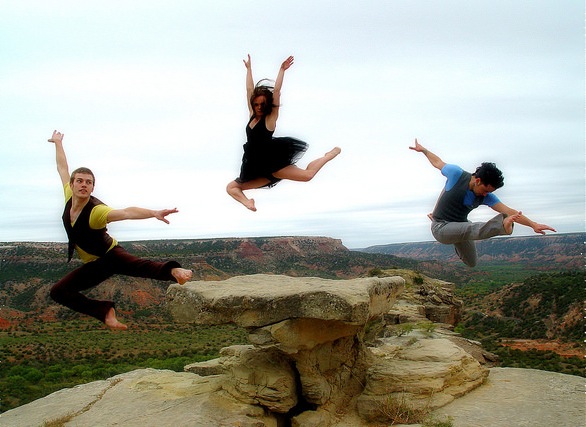 Three dancers leaping off the ground in a canyon.